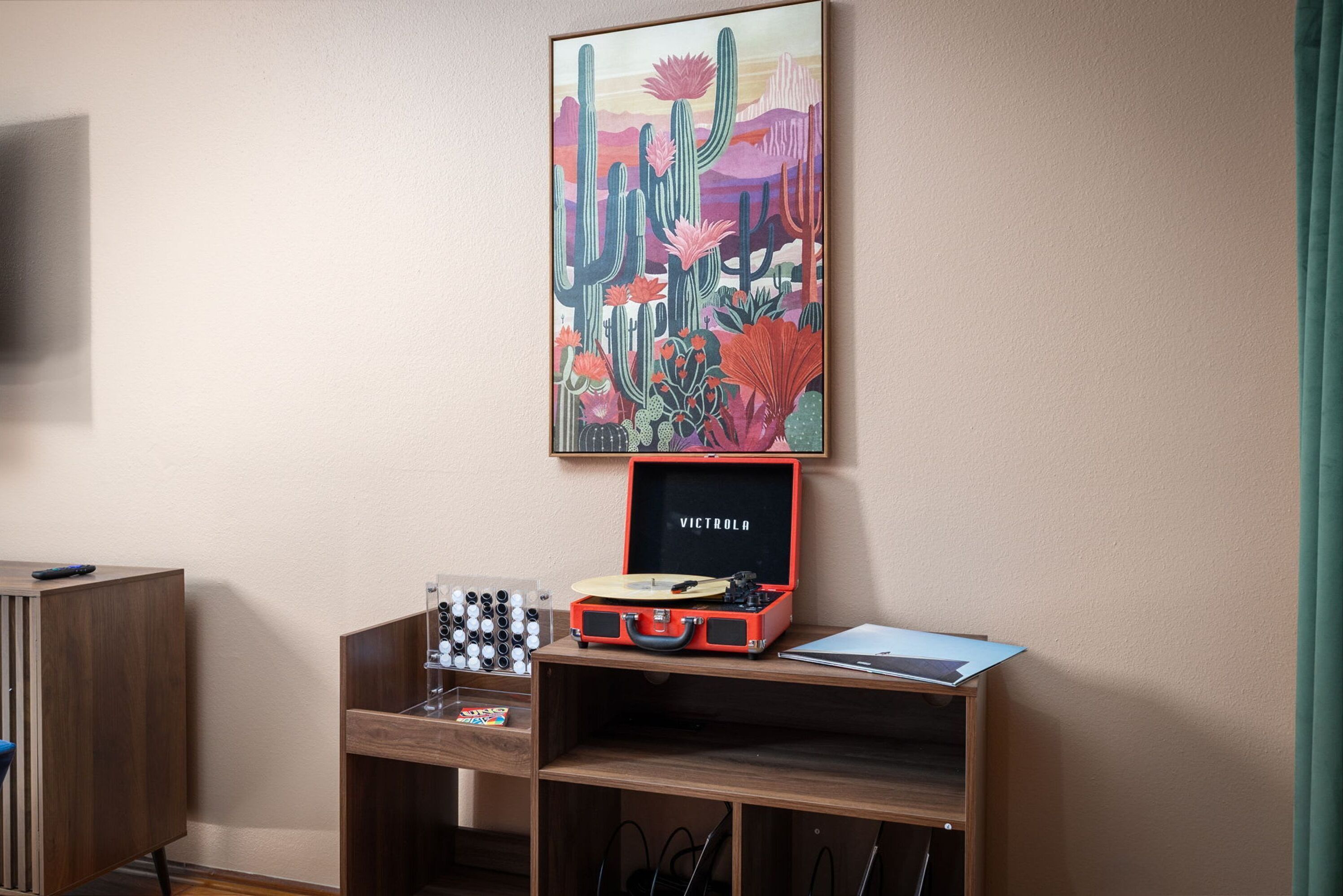 A room with a wooden desk, a red suitcase, and a framed artwork on the wall.