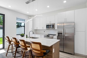 Uma cozinha moderna com armários brancos, eletrodomésticos de aço inoxidável e uma ilha central com banquetas.