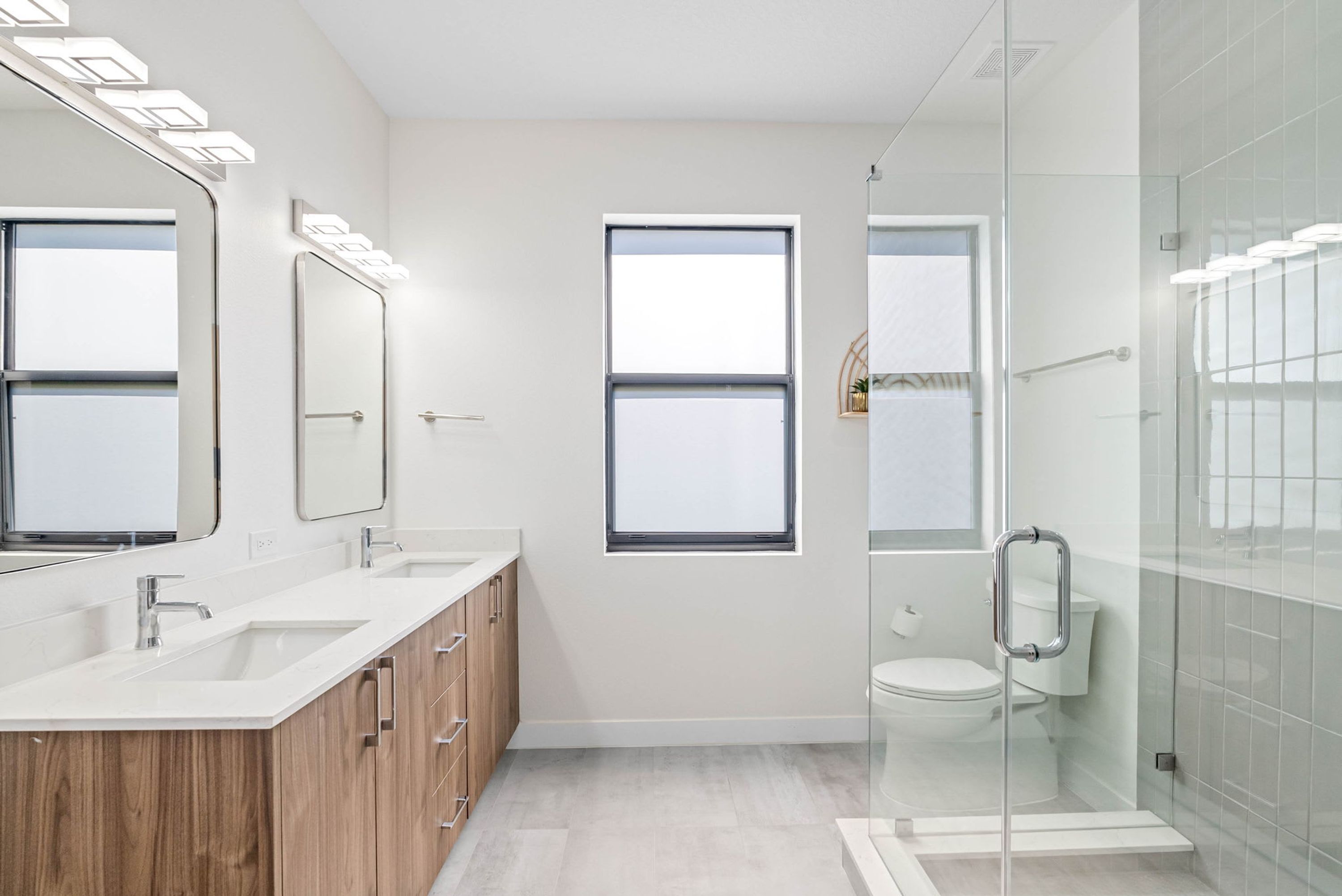 Een moderne badkamer met een dubbele wastafel, een grote spiegel, een raam en een douchecabine met glazen wanden.