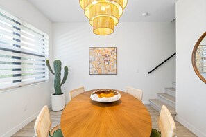 Un espace de salle à manger moderne avec une table en bois, des chaises, une plante succulente, un lustre et un escalier.
