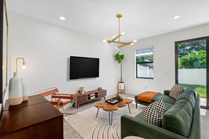 A modern living room with a flat-screen TV, a green sofa, a wooden coffee table, and a unique ceiling light fixture. - Close to DT Tampa Newly Designed Town Home (Tampa)