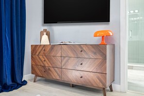 Ein modernes Badezimmer mit einem Holzschrank, einem flachbildfernseher darüber und einem sichtbaren Duschbereich zur rechten Seite.