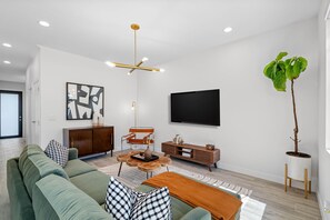 Ein modernes Wohnzimmer mit einem grünen Sofa, einem Couchtisch, einem Fernseher und einer Pflanze.
