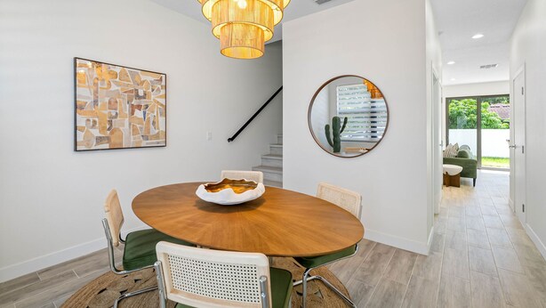 A dining area with a round table, chairs, a hanging light fixture, a framed abstract painting, a round mirror, and a staircase. - Close to DT Tampa Newly Designed Town Home (Tampa)