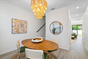 A dining area with a round table, chairs, a hanging light fixture, a framed abstract painting, a round mirror, and a staircase. - Close to DT Tampa Newly Designed Town Home (Tampa)