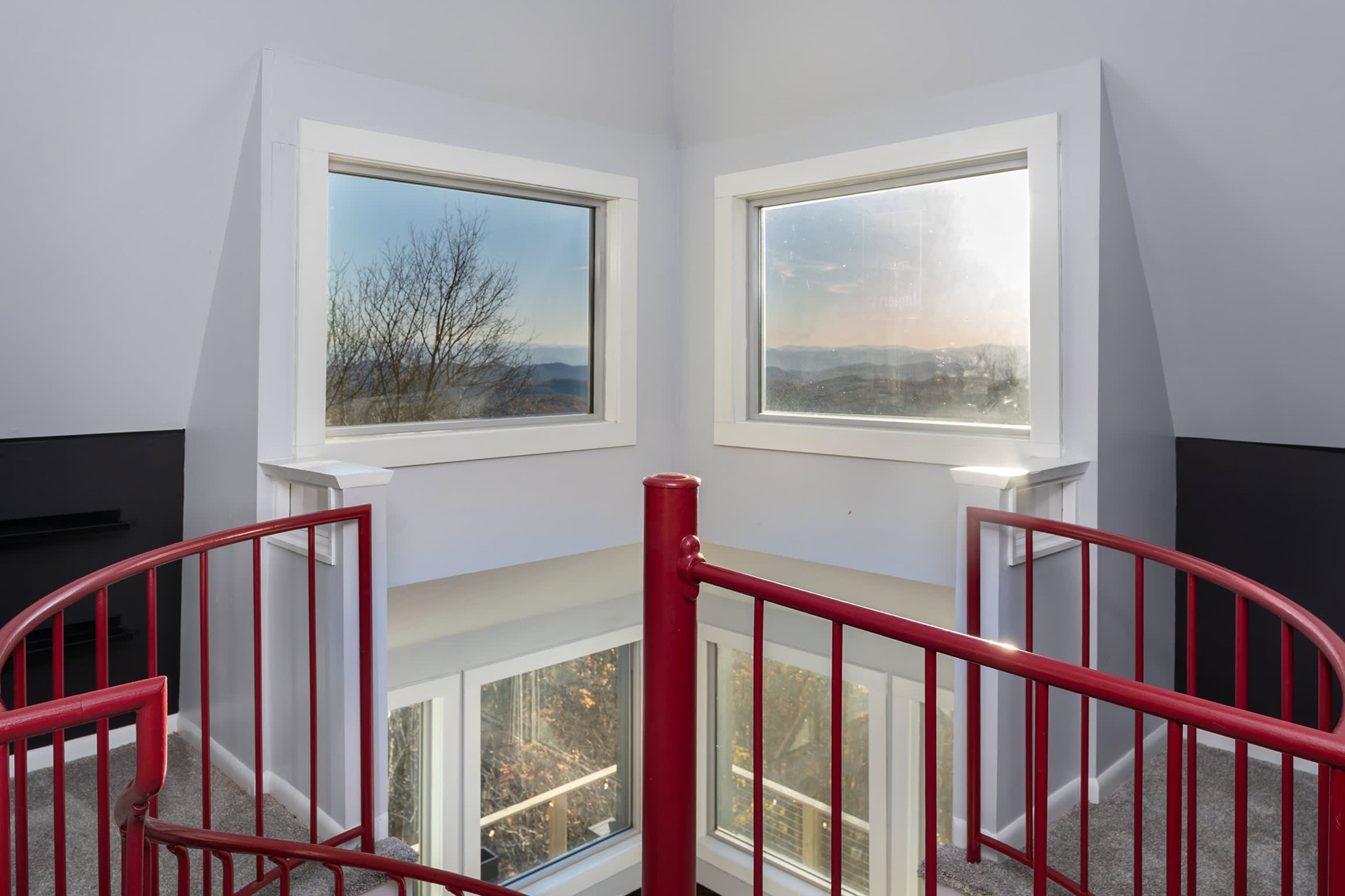 A corner room with two windows overlooking a landscape, a red railing, and a carpeted floor.