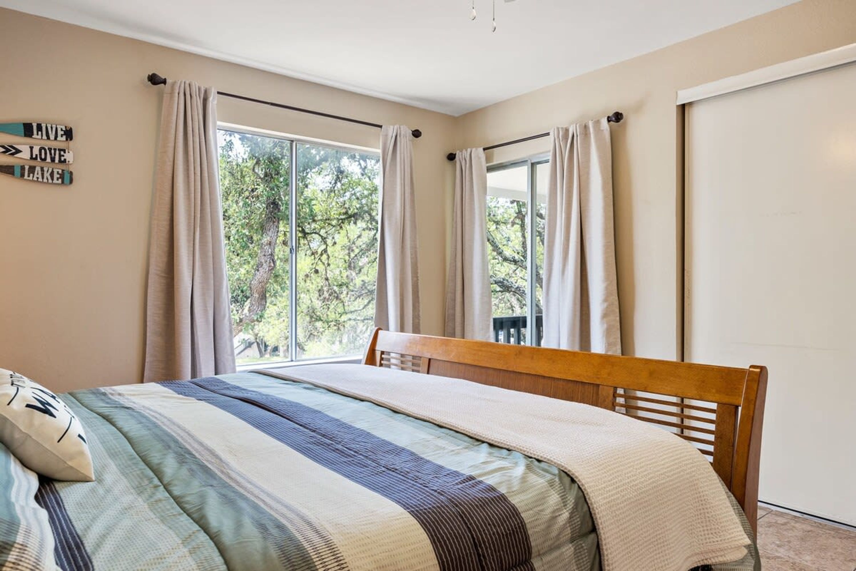 Une chambre à coucher avec un lit, une fenêtre avec des rideaux et une vue sur les arbres à l’extérieur.