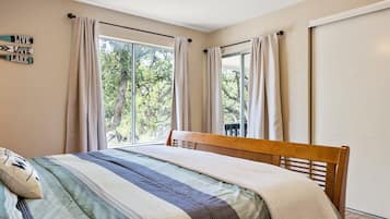 A bedroom with a bed, a window with curtains, and a view of trees outside.