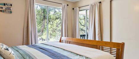 Une chambre à coucher avec un lit, une fenêtre avec des rideaux et une vue sur les arbres à l’extérieur.