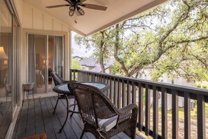 Un espacio al aire libre techado con muebles de mimbre, un ventilador de techo y vistas a árboles y una casa.