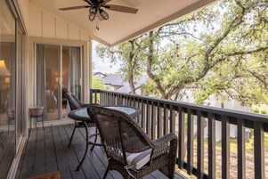 Un espacio al aire libre techado con muebles de mimbre, un ventilador de techo y vistas a árboles y una casa.