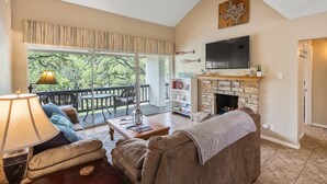 Un salon avec une cheminée, un téléviseur et un balcon donnant sur la forêt.