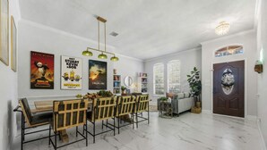 A dining area with a marble floor, wooden chairs, a bench, and a table. There are posters on the wall, a ceiling light fixture, and a door with a decorative glass panel. - 4 Themed Rooms 11 Min to Universal Kids (Frisco)