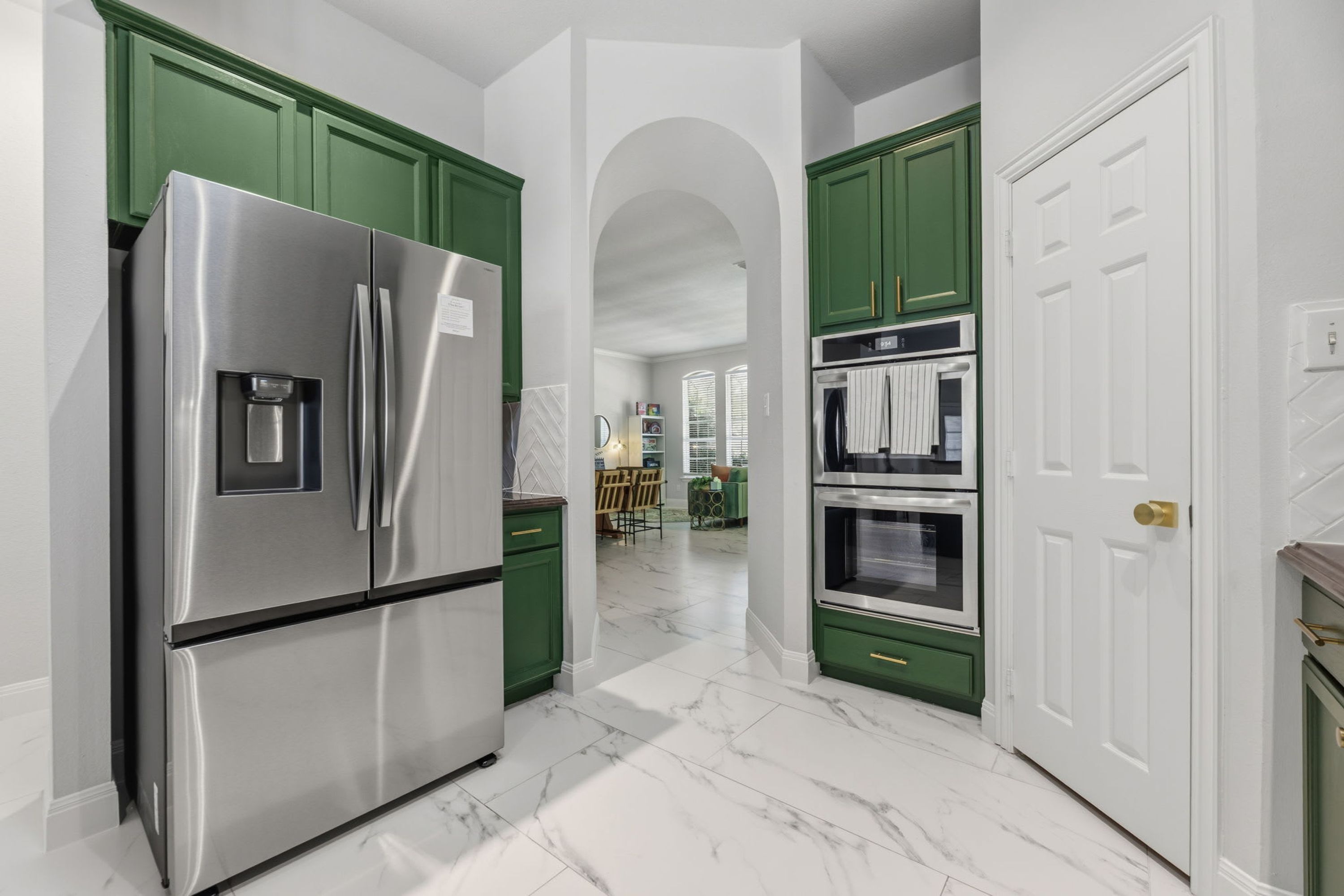 A kitchen with stainless steel appliances, green cabinets, and a white door.