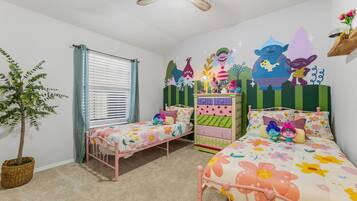 Quarto infantil com duas camas, um penteou e um ventilador de teto, além de uma janela com persianas.