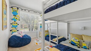 A bunk bed room with a Minion-themed wall decoration, a bean bag chair, and a window with blinds. - 4 Themed Rooms 11 Min to Universal Kids (Frisco)