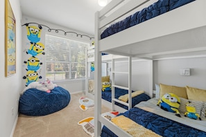 Ein Mehrbettzimmer mit Minion-Wanddekoration, einem Sitzsack und einem Fenster mit Jalousien.