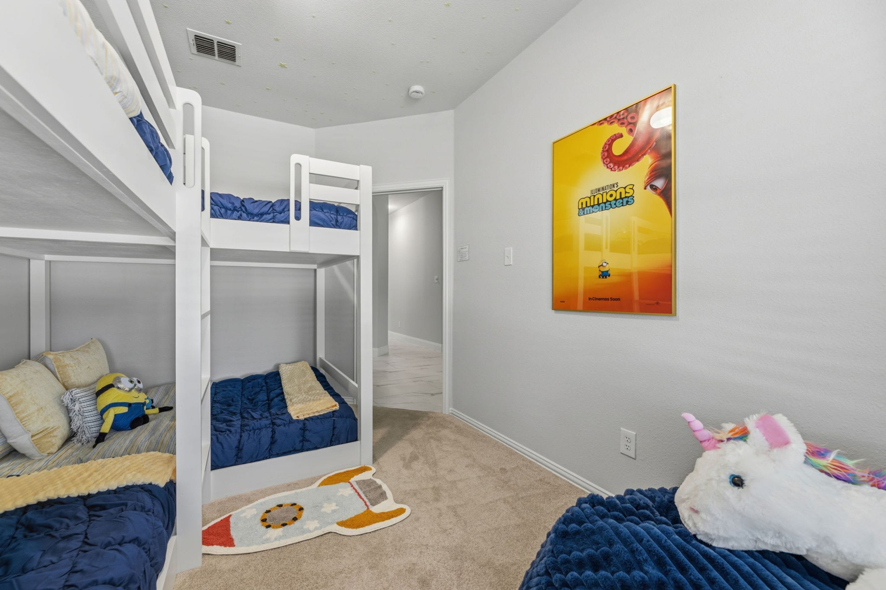 Een kinderkamer met stapelbedden, een Minion knuffel, eenhoorn knuffel en een film poster aan de muur.