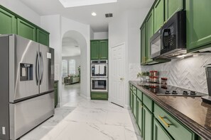 A modern kitchen with green cabinets, stainless steel appliances, and a herringbone tile backsplash. - 4 Themed Rooms 11 Min to Universal Kids (Frisco)