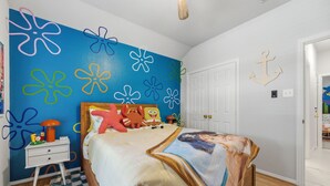 A bedroom with a bed, a nightstand, a wall with flower patterns, and a door with an anchor decoration. - 4 Themed Rooms 11 Min to Universal Kids (Frisco)