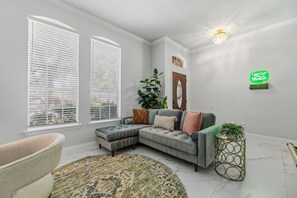 A room with a sectional sofa, a round rug, a plant, and a wall-mounted light fixture. - 4 Themed Rooms 11 Min to Universal Kids (Frisco)
