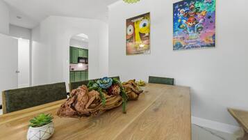 Uma sala de jantar com uma mesa de madeira, cadeiras, um centro de mesa e dois quadros na parede.