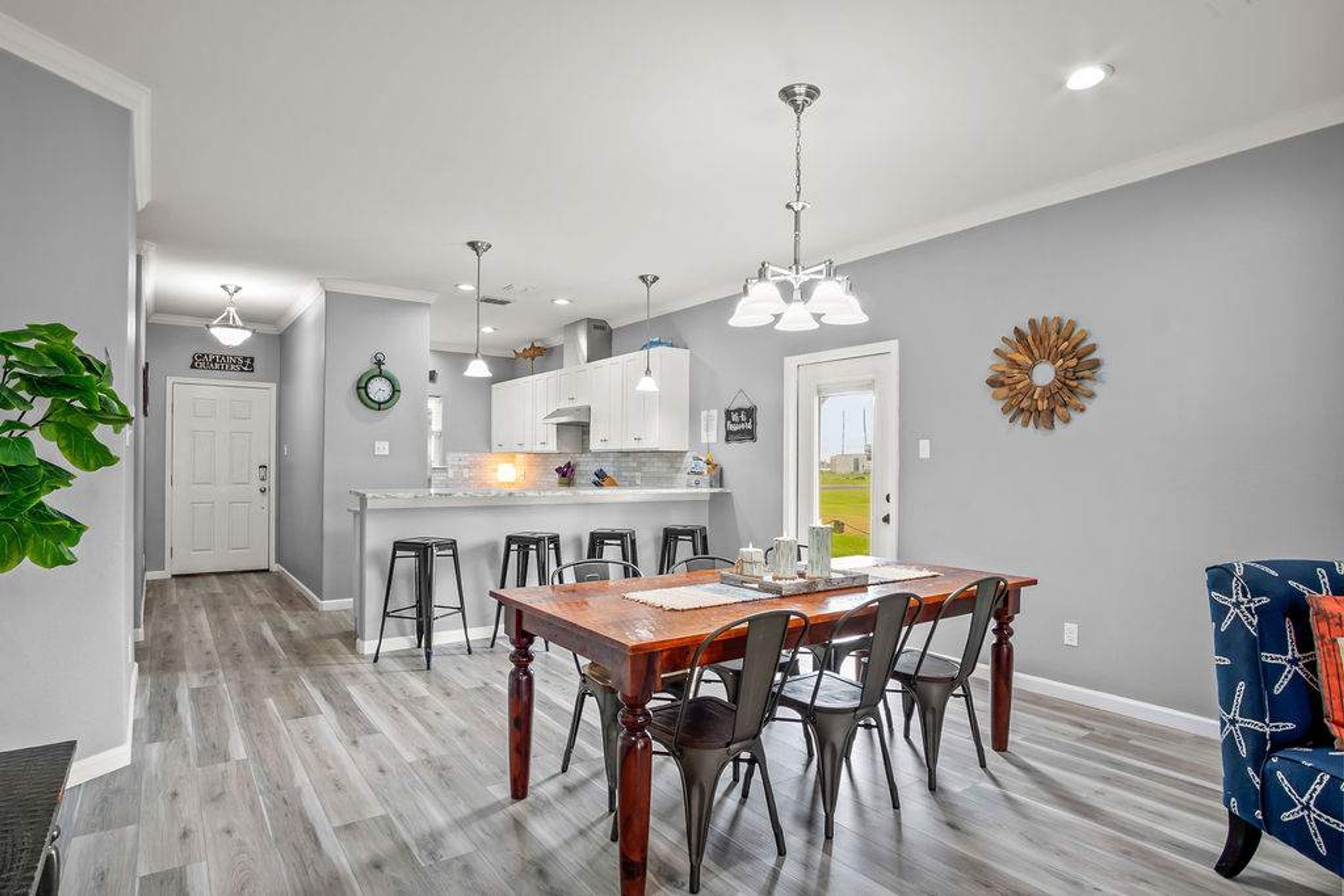 A spacious kitchen with a central island, modern pendant lighting, and a dining area with a wooden table and metal chairs.