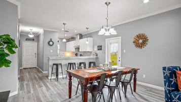 A spacious kitchen with a central island, modern pendant lighting, and a dining area with a wooden table and metal chairs.
