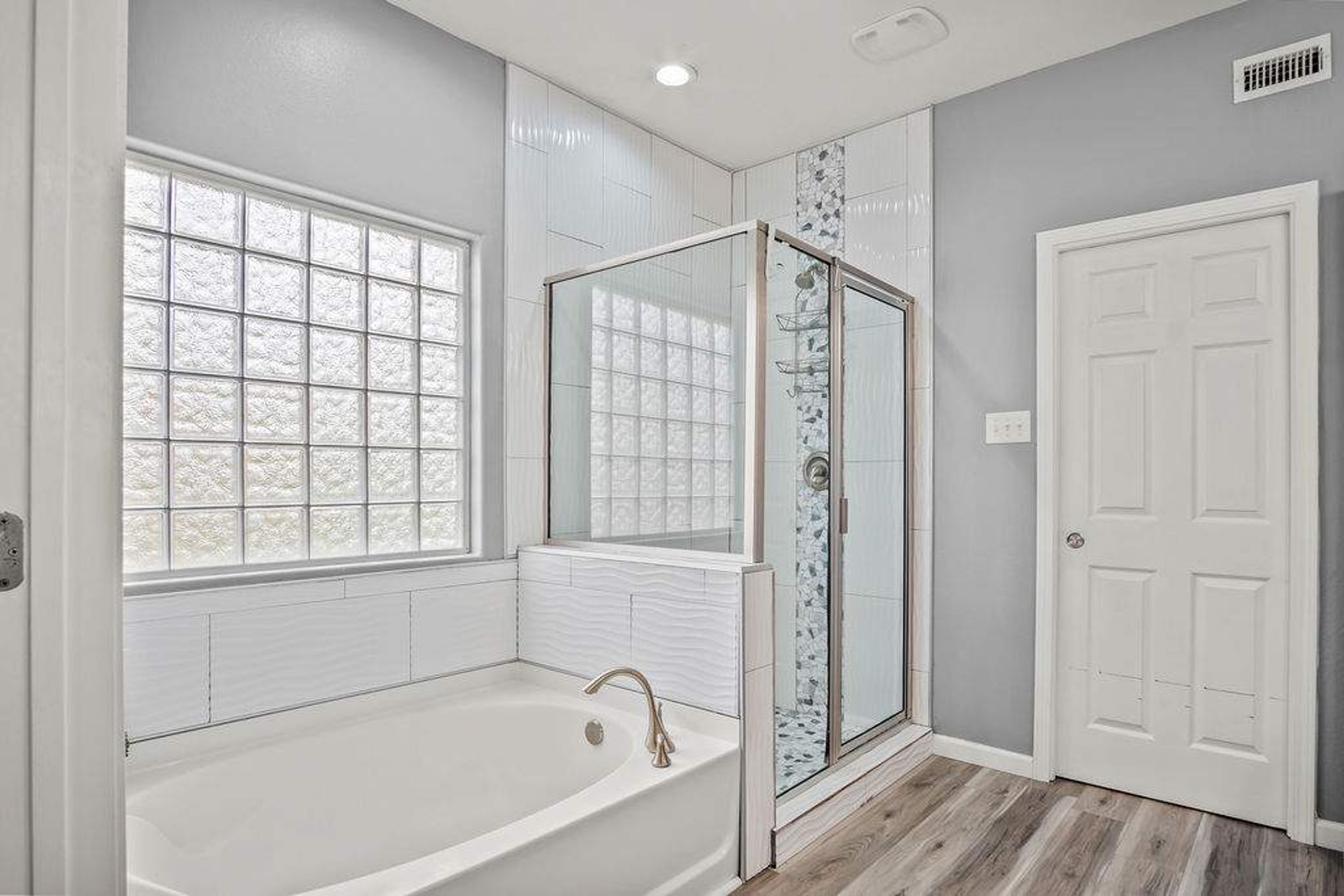 A bathroom with a bathtub, a shower enclosure, and a window.