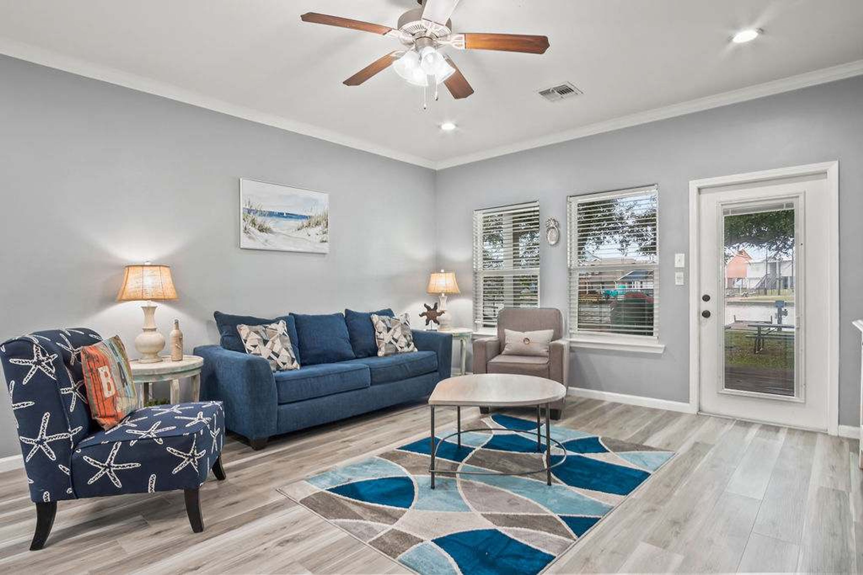 A living room with a blue sofa, a round coffee table, a chair with starfish upholstery, and a ceiling fan.