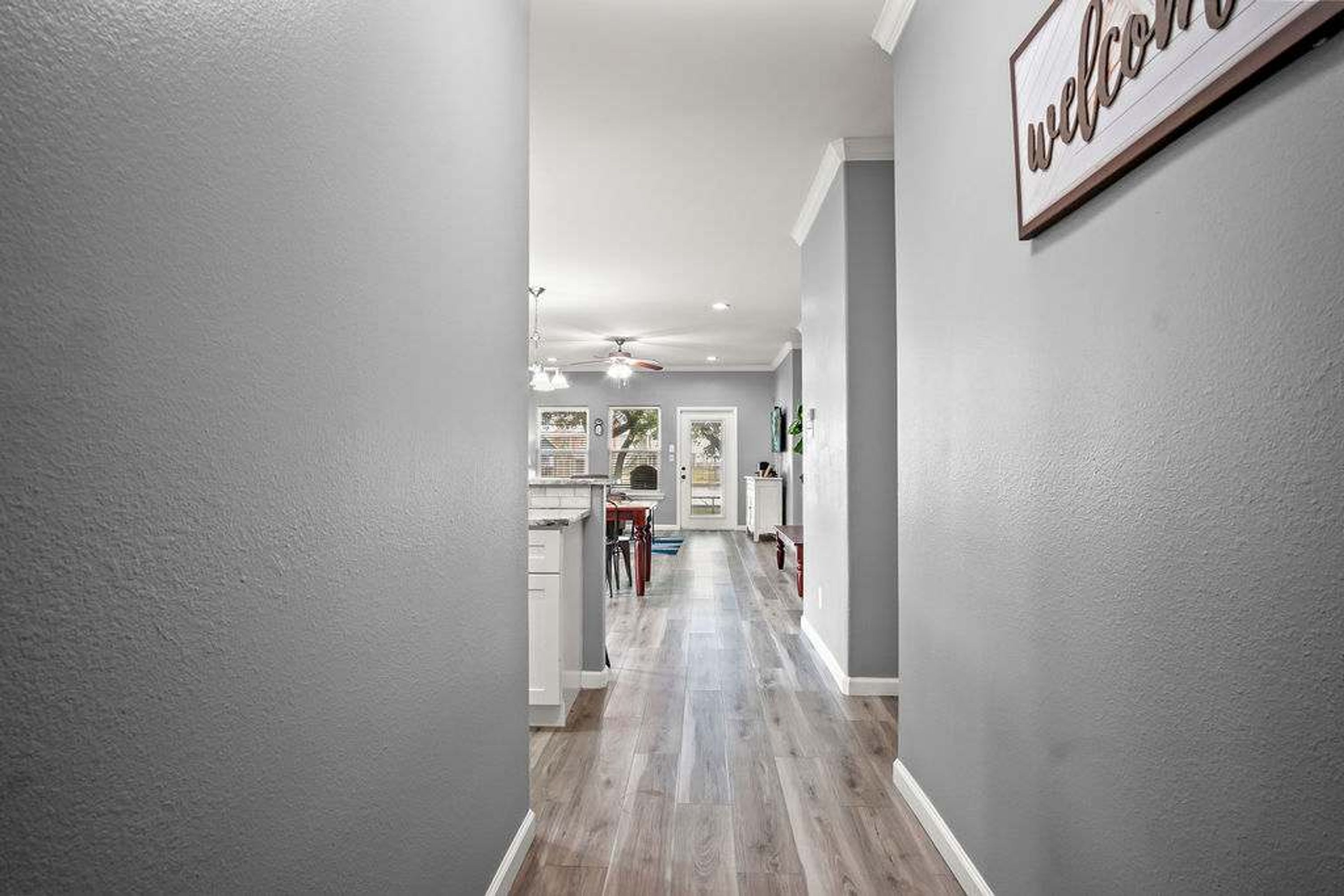 A hallway with a welcome sign, wooden flooring, and a ceiling fan.