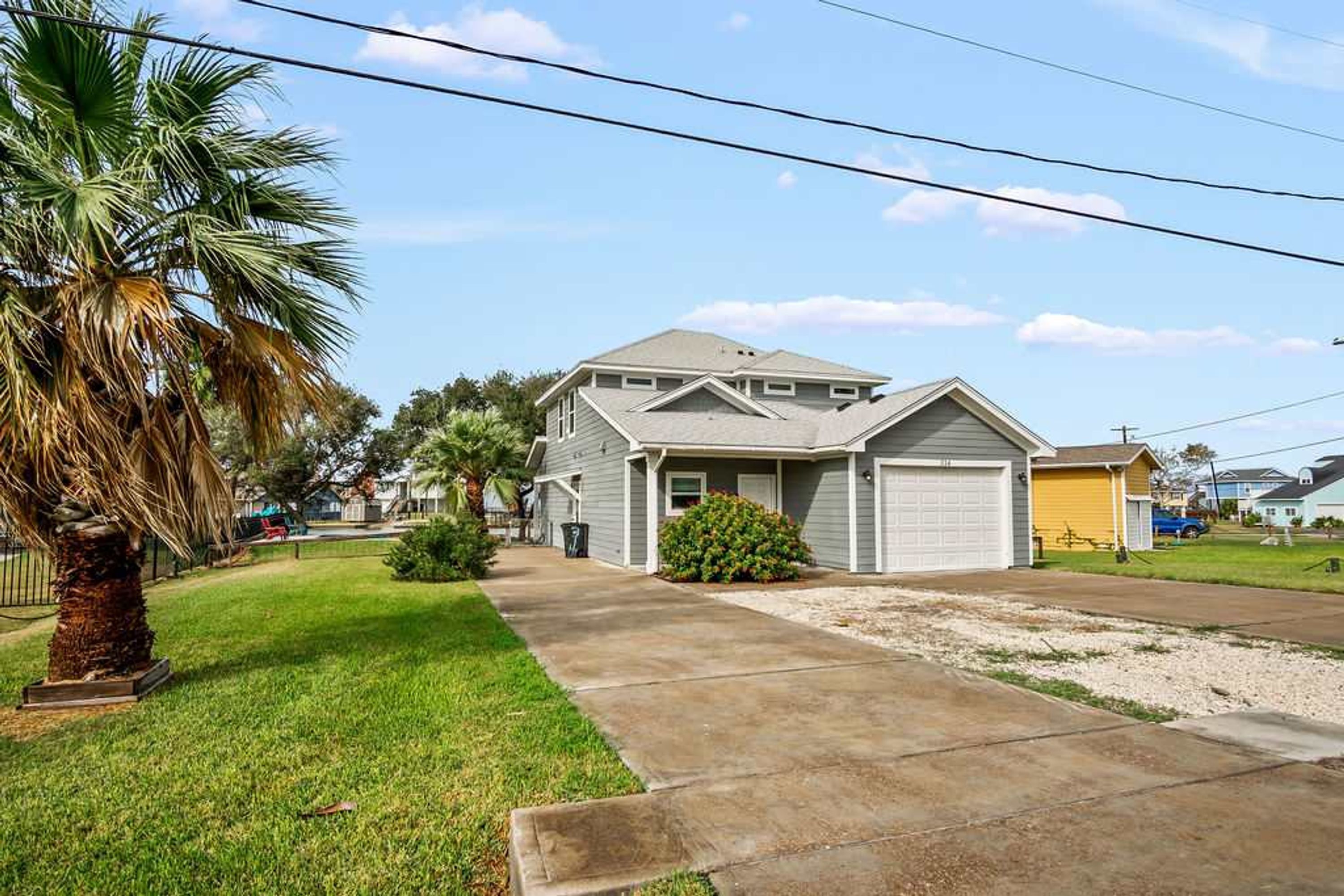 A residential house with a garage, a driveway, and a well-maintained lawn with a palm tree.