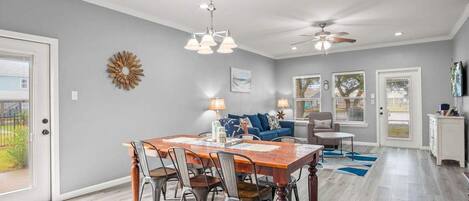 A dining area with a wooden table and chairs, a ceiling fan, and a chandelier.
