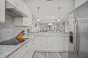 Una cocina moderna con armarios blancos, un refrigerador de acero inoxidable y una encimera de granito.
