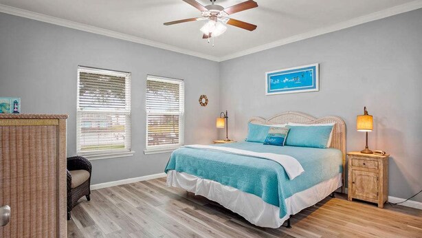 Um quarto com cama, duas mesas de cabeceira, um ventilador de teto e duas janelas com persianas.