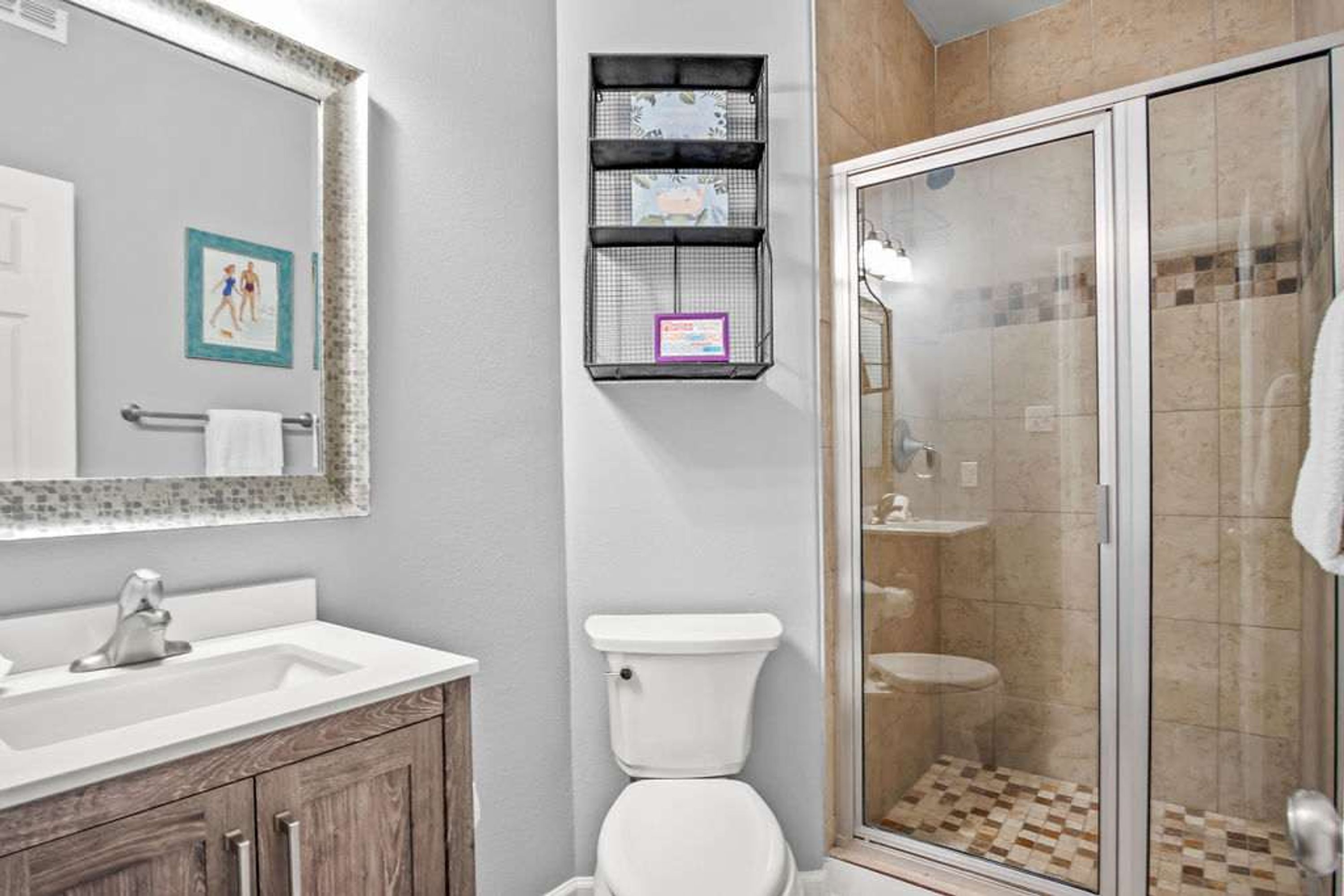 A bathroom with a white sink, a toilet, a shower enclosure, and a mirror with a decorative frame.
