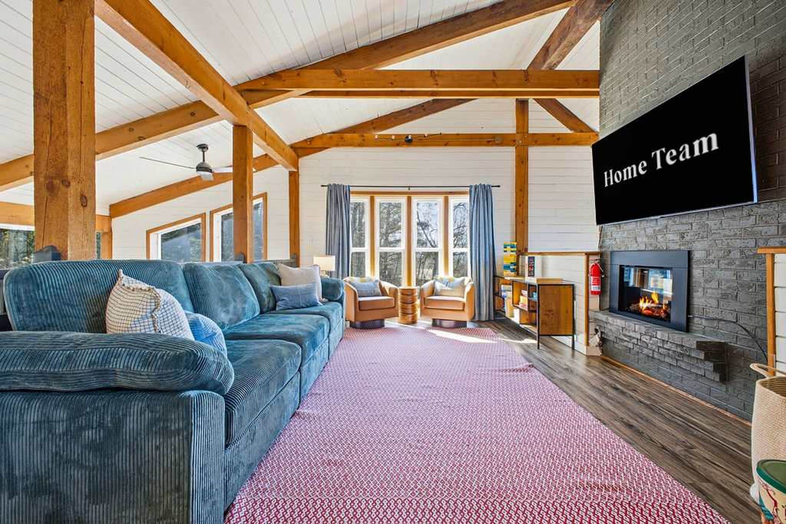 A spacious living room with a large blue sectional sofa, a fireplace, and a sign reading 'Home Team'.