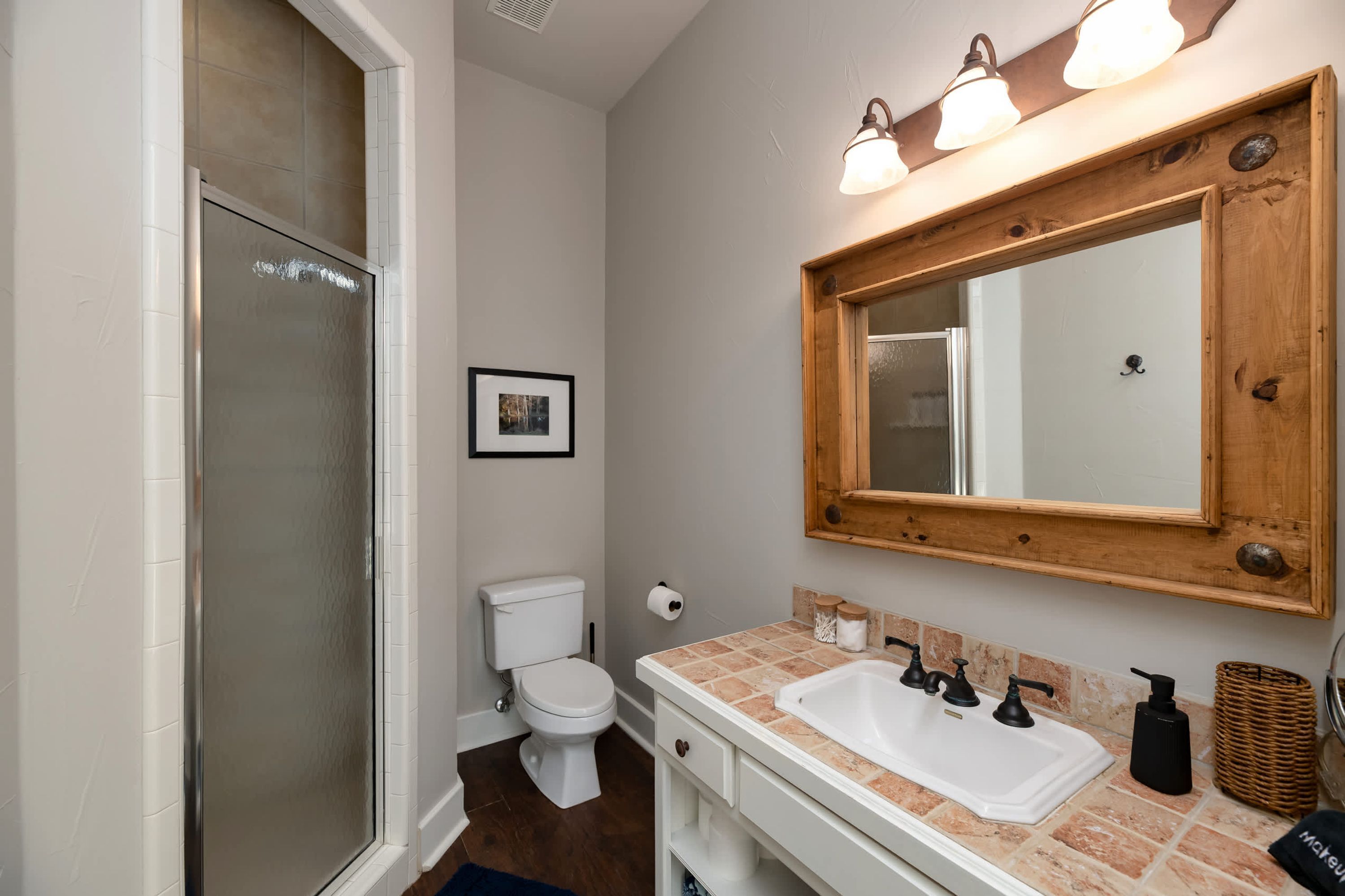 A bathroom with a shower, toilet, sink, and a large mirror with lights.