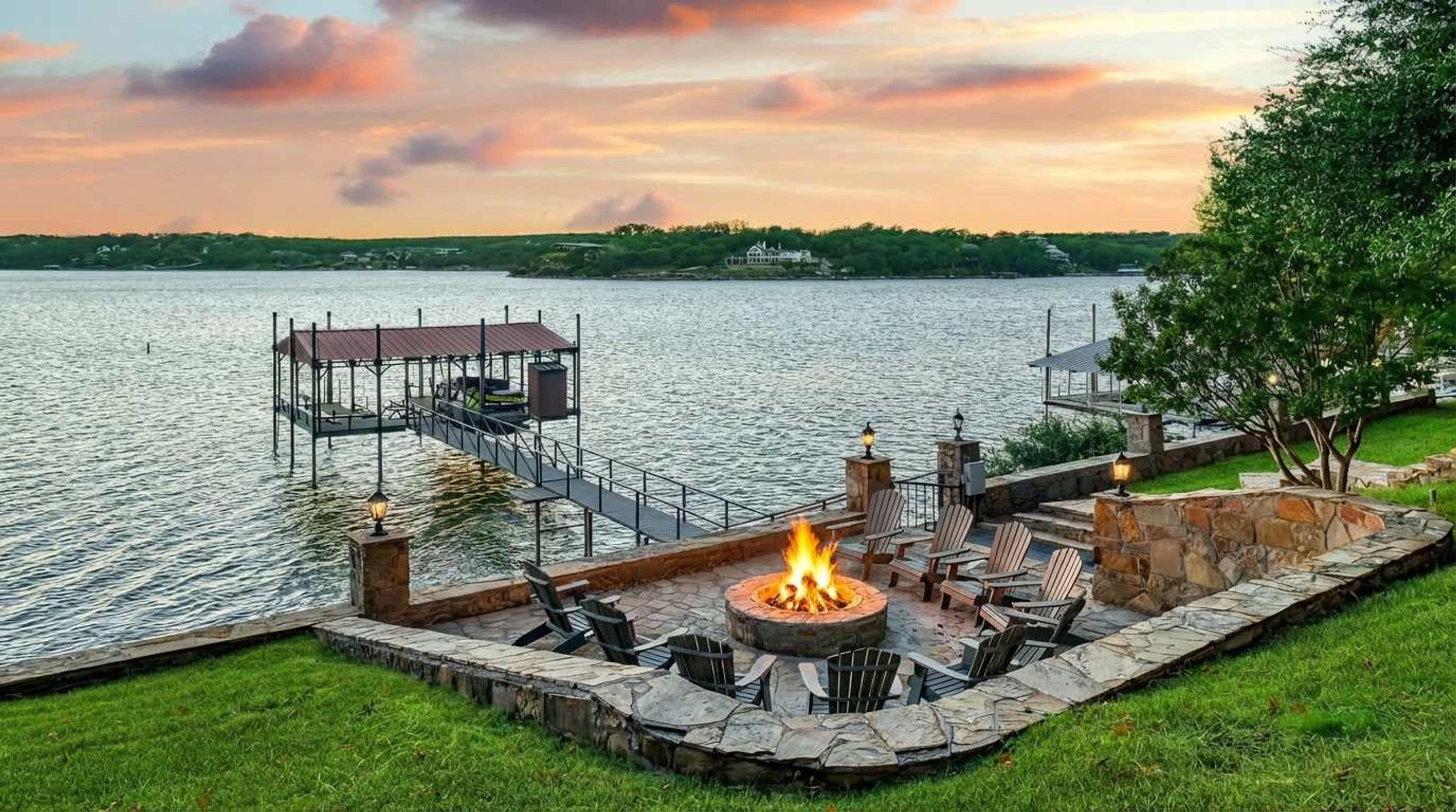 A lakeside deck with a fire pit and outdoor seating, surrounded by stone walls and a dock extending into the water.