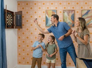 Eine Familie spielt Darts in einem Raum mit gestreiftem Wandpapier und abstrakten Kunstwerken an den Wänden.