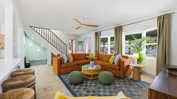 A modern living room with a curved sofa, a ceiling fan, a dining area with a white table, and a staircase.