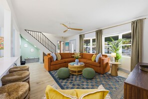En moderne stue med en buet sofa, en loftventilator, et spiseområde med et hvidt bord og en trappe.
