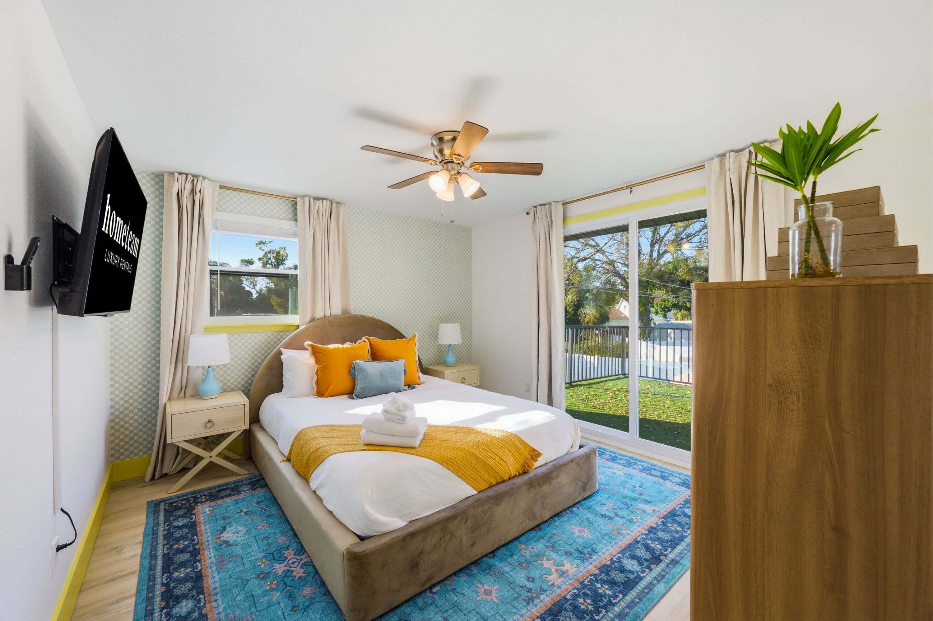 A bedroom with a bed, bedside tables, a ceiling fan, a window, and a view of the outdoors.
