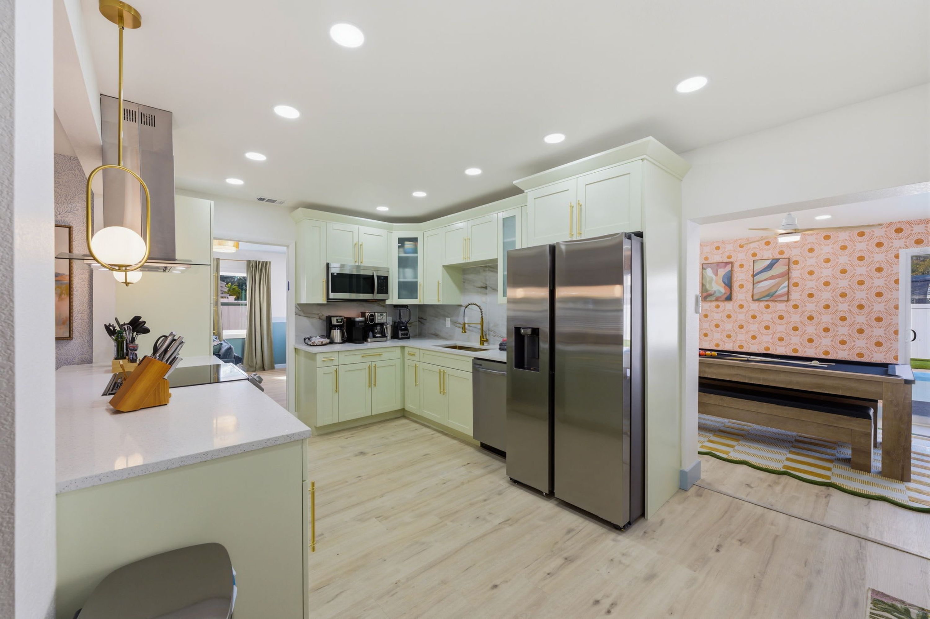 A modern kitchen with light green cabinets, stainless steel appliances, and a central island with a sink.