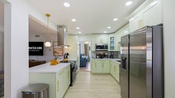 A modern kitchen with stainless steel appliances, light green cabinets, and a central island with a sink and countertop.