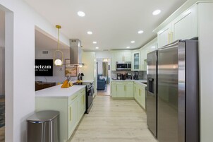 Una cocina moderna con electrodomésticos de acero inoxidable, armarios verde claro y una isla central con pileta y encimera.