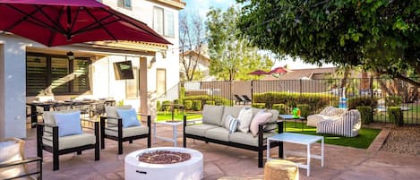 An outdoor patio area with a dining table, chairs, a sofa, and a fire pit.