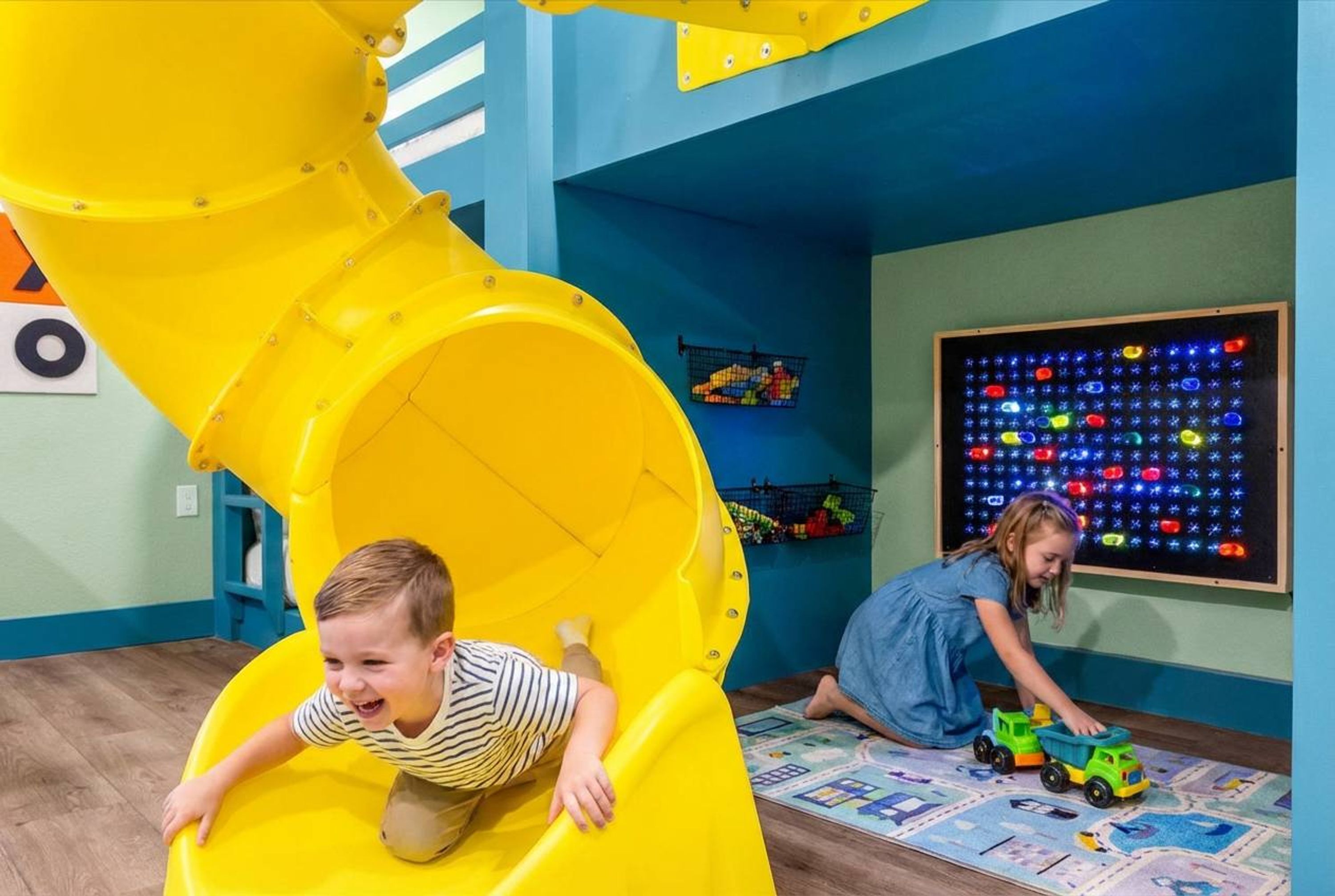 Children playing on a yellow slide and a play mat with toys.