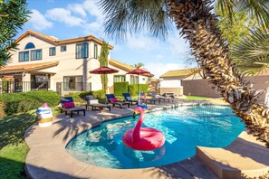 A swimming pool with a flamingo float, surrounded by lounge chairs and umbrellas, with a house in the background. - Epic Family Getaway Sport Court Heated Pool (Scottsdale)
