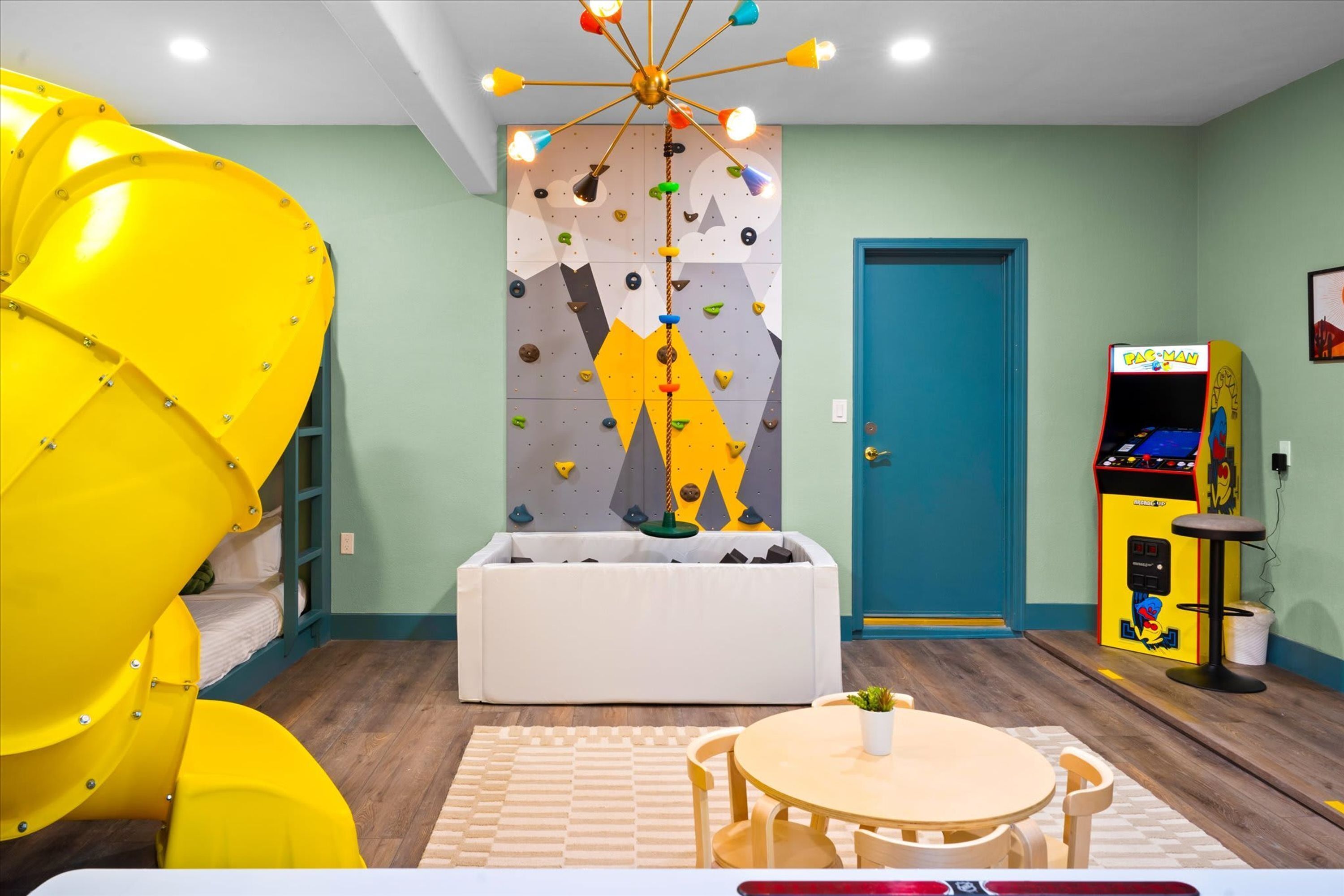 Une pièce avec un mur d’escalade, une borne d’arcade Pac-Man et un canapé blanc.